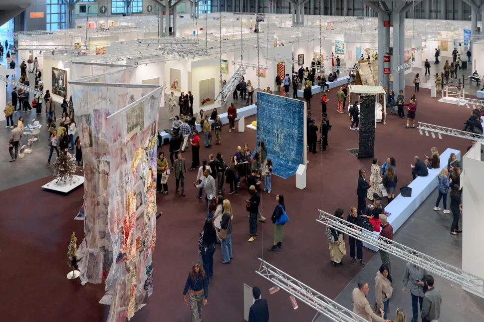 A wide view of The Armory Show floor shows visitors moving among gallery booths and large-scale suspended and freestanding installations.