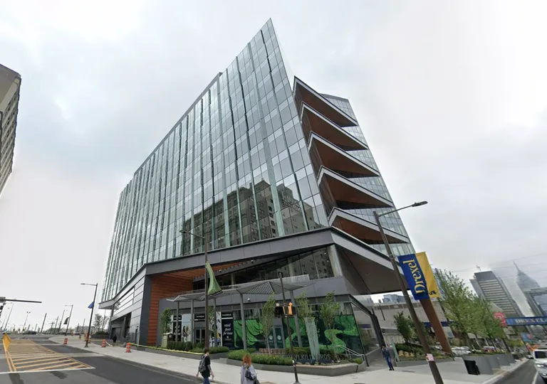 A modern glass building with an angled architectural design, located on a city street with pedestrians and a visible Drexel banner.