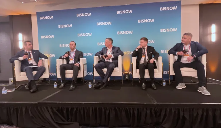 Five people in business attire sitting on stage chairs, participating in a panel discussion at the Bisnow event, with a brand background.
