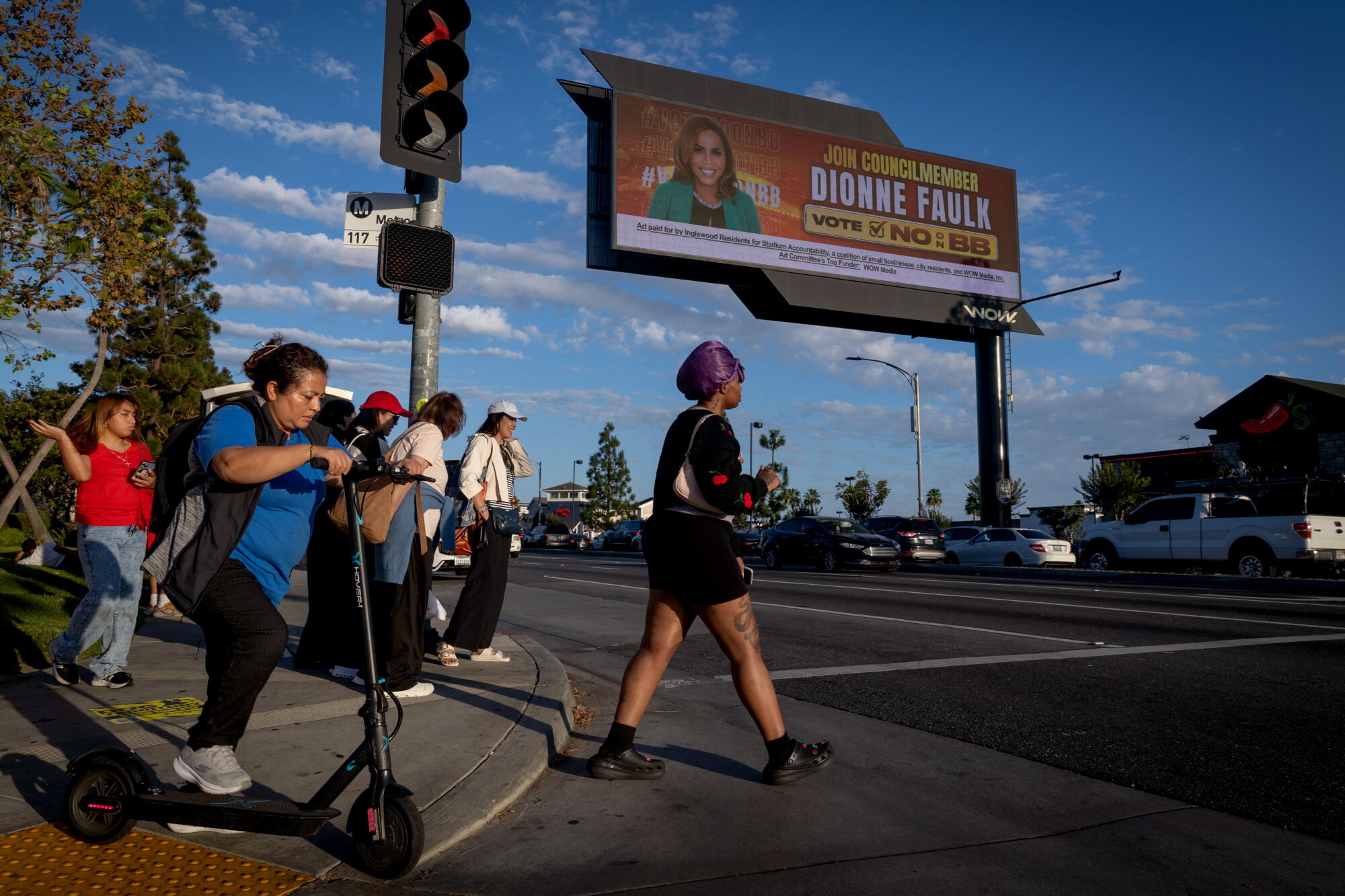 People walk across Century Avenue, near Inglewood's electronic billboards.