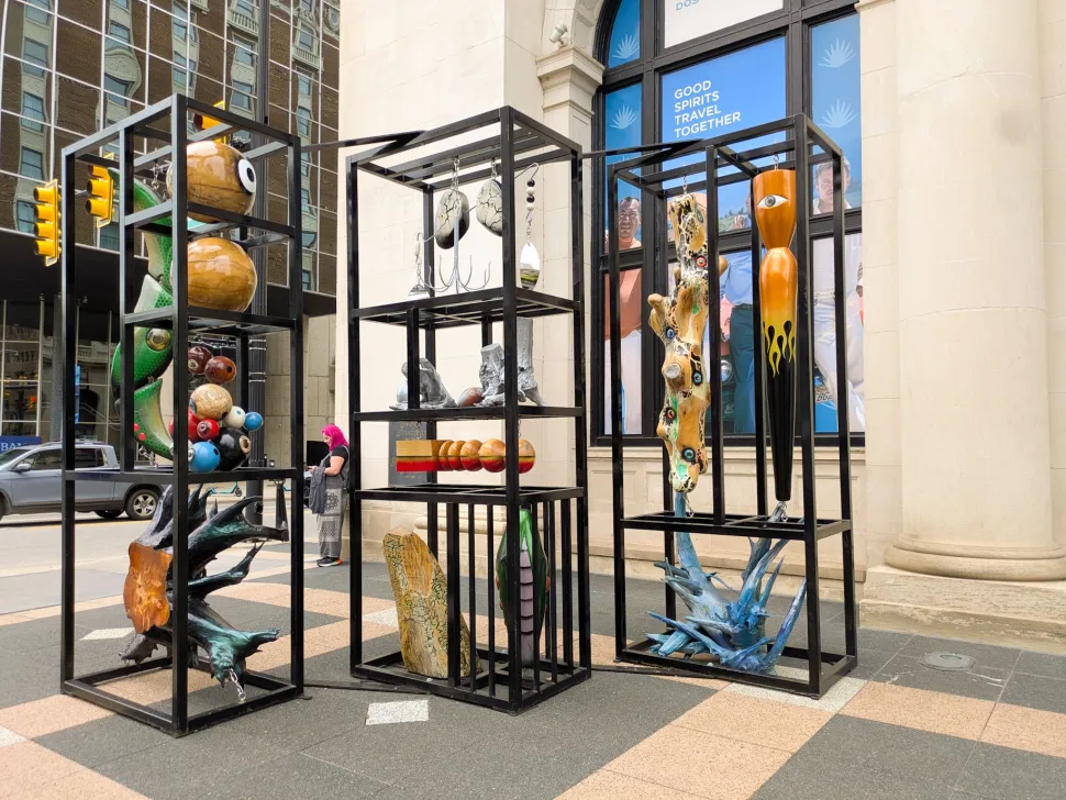 An outdoor art installation in Grand Rapids features colorful sculptural forms displayed inside tall black metal frames along a downtown sidewalk.