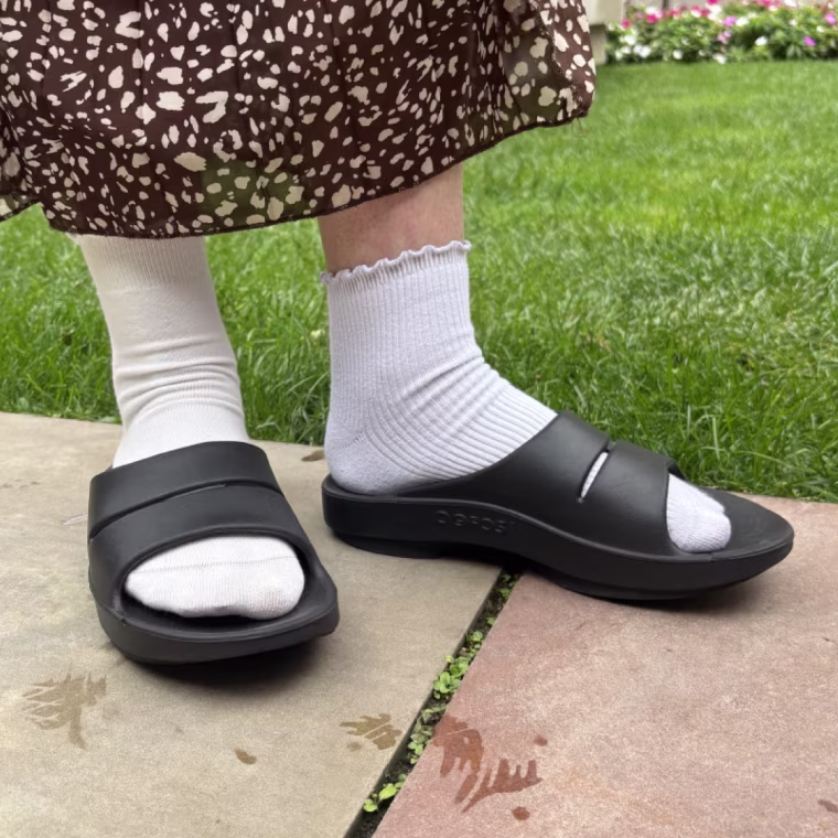 A woman wearing a pair of Oofos OOyea Recovery Slides.